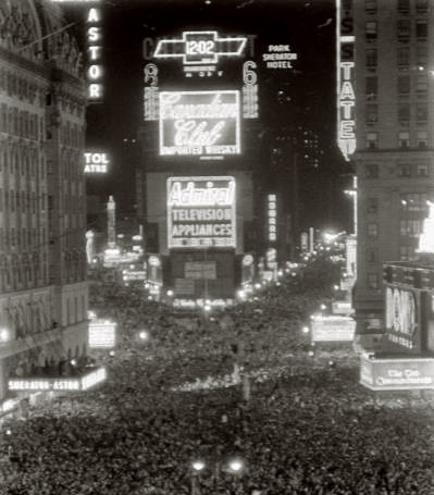 A large crowd gathers at night in Times Square, New York City, surrounded by bright neon signs and animated advertisements.