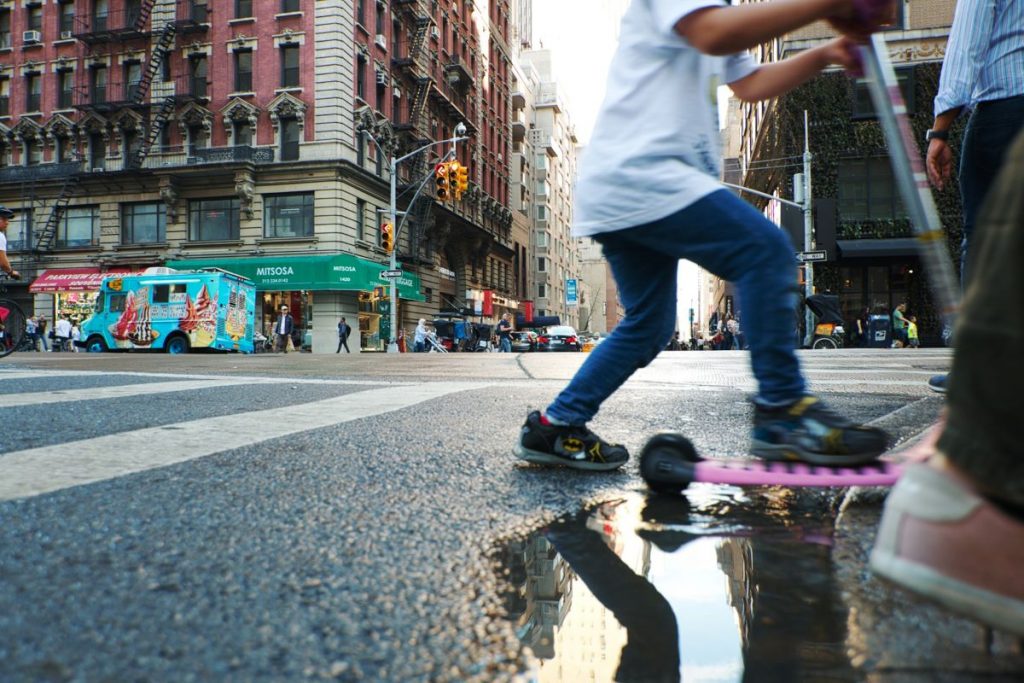 A boy on a scooter crossing the crosswalk in SoHo. 