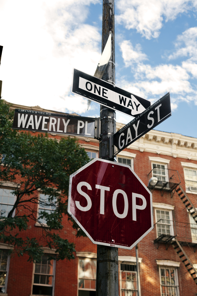 A stop sign and one-way sign mark the corner of Waverly Place and Gay Street, Greenwich Village, beside a red brick building.