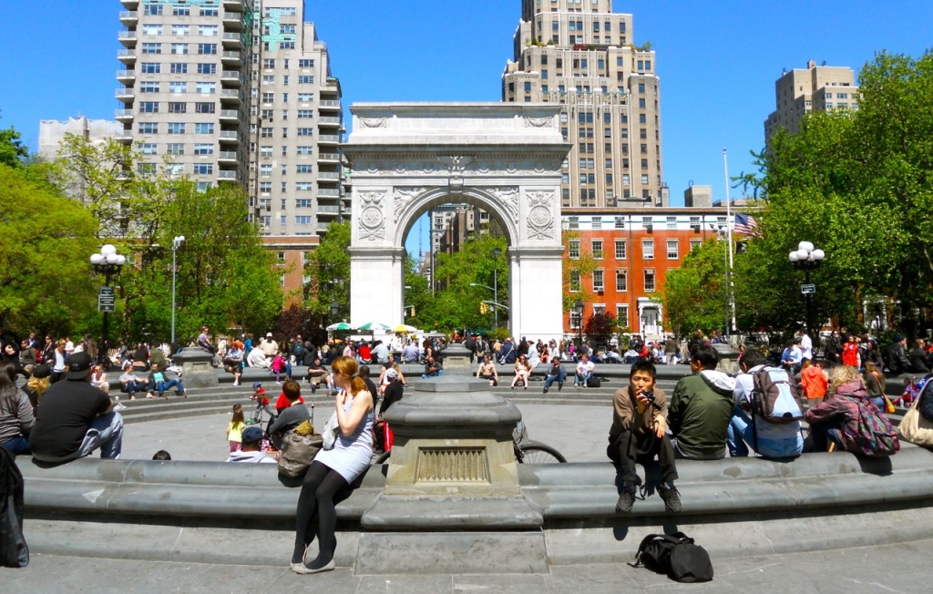 People gather around the fountain at Washington Square Park, relaxing beneath the Washington Square Arch with city buildings behind.