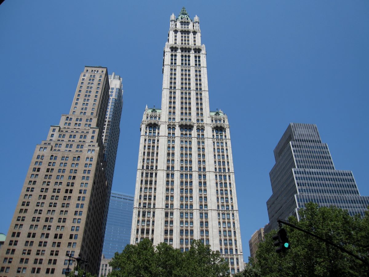 Tall New York skyscrapers tower over a historic, ornate building, surrounded by modern high-rises and leafy green trees below.