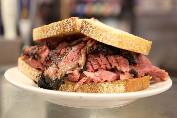 A thick pastrami sandwich stacked on seeded rye bread sits on a white plate, served at Katz’s Delicatessen, New York City.