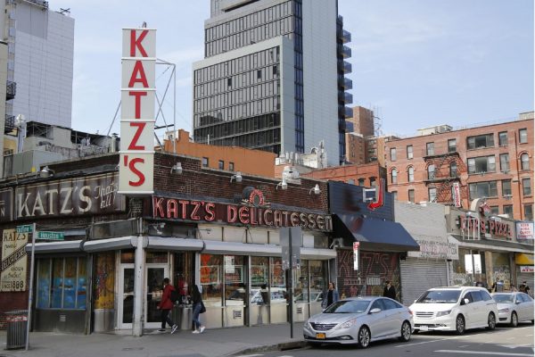 Pedestrians enter Katz’s Delicatessen on New York Citys Lower East Side, passing its iconic red sign and brick storefront.