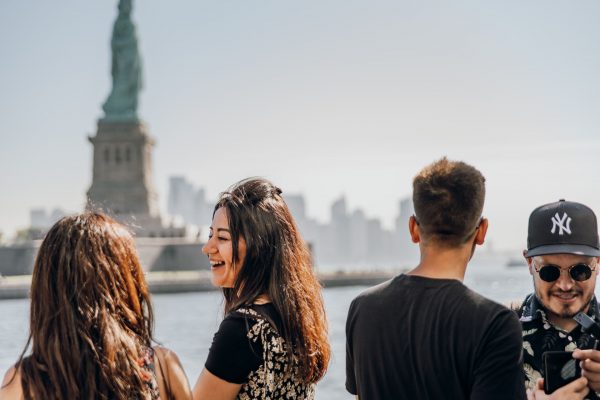 Four friends stand by the waterfront in Lower Manhattan. A woman laughs as a man in a Yankees cap looks at his phone.