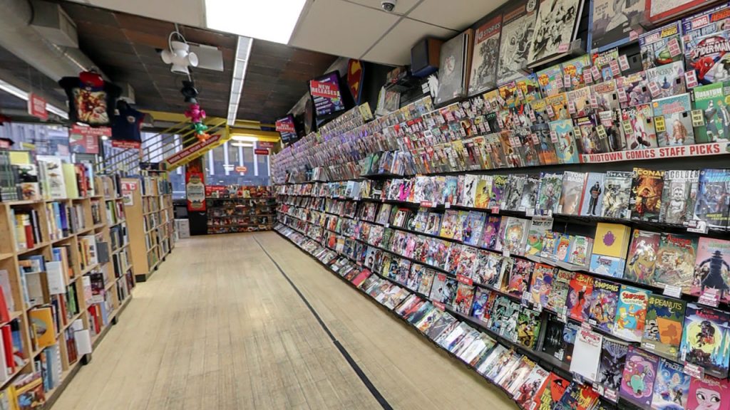 Several customers browse long shelves of colorful comics at a bright, organized NYC comic book store with posters and wooden floors.