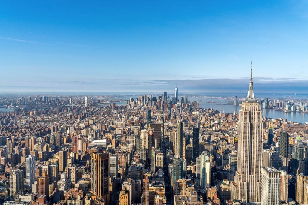 Aerial view of New York City skyline with the Empire State Building on the right under clear blue skies.