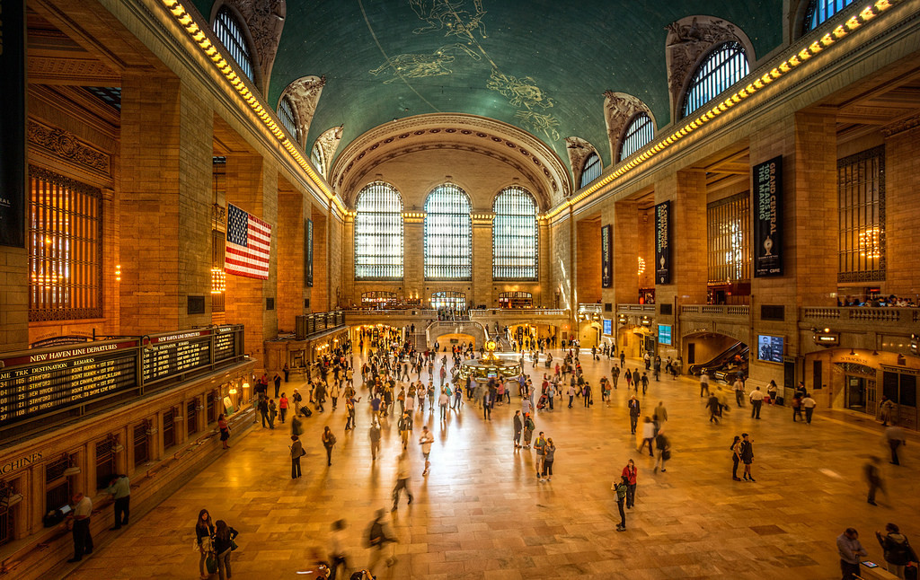 People hurry across Grand Central Terminal’s main concourse as sunlight pours through arched windows and the constellation-painted turquoise ceiling shines.