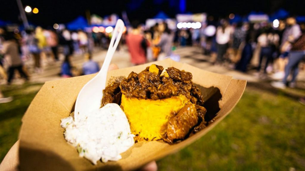 A person holding up food from the Queens night market. 