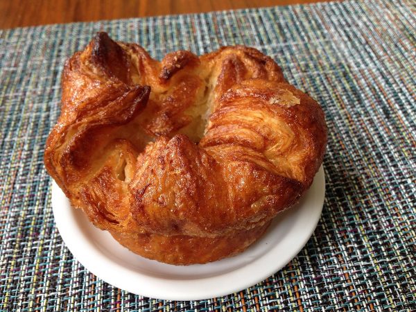 An Kouign amann pastry sitting on a white plate ready to eat