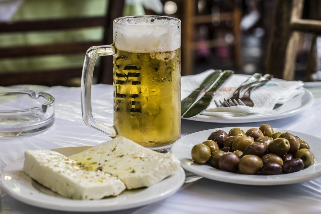Greek table with feta cheese, a plate of olives, and a frosty beer