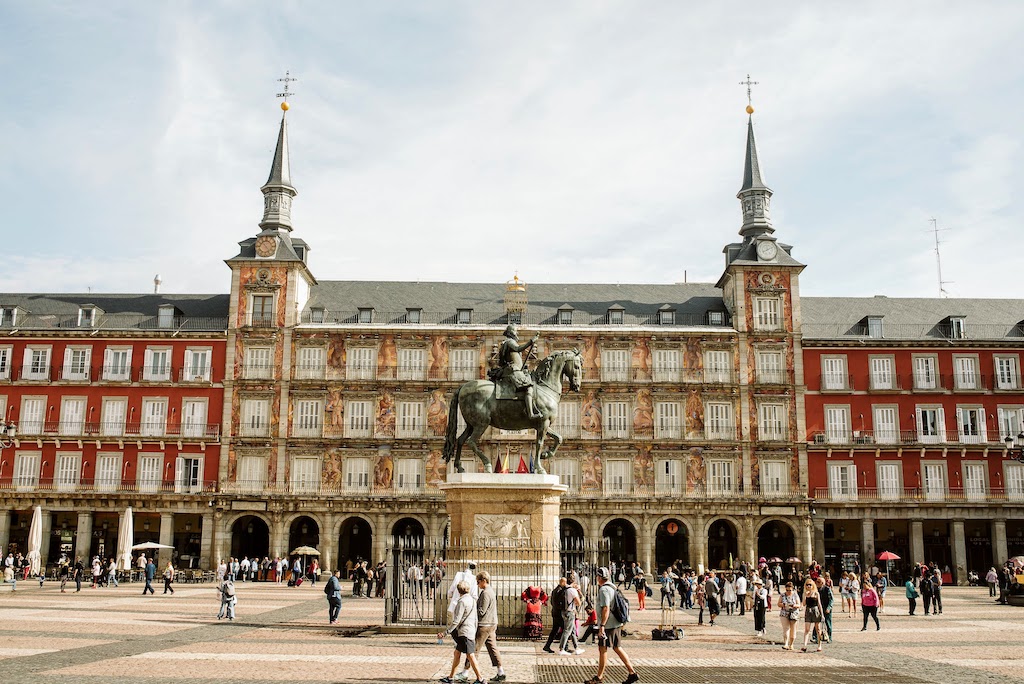 Visitors walk through Madrid's main square (Plaza Mayor) on a bright summer day