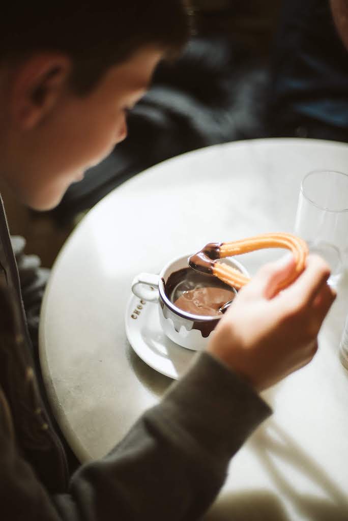 Young boy dipping a freshly fried churro into a mug of Spanish hot chocolate at a restaurant in Madrid, Spain