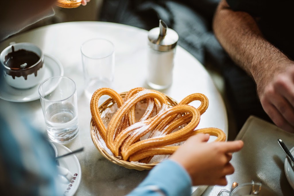 Child reaching for a churro from a communal basket of churros blanketed with a dusting of sugar