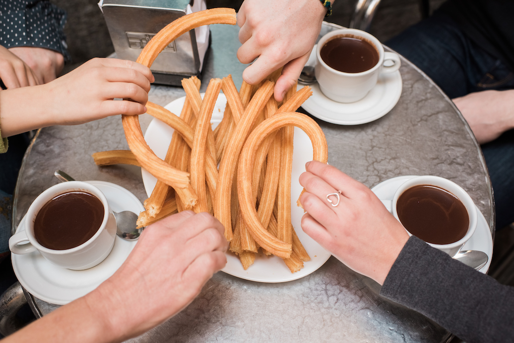 4 people sharing a plate of churros around a table with mugs of hot chocolate in Spain