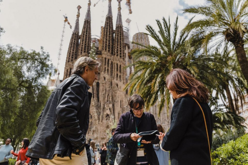 A pair of guests stand next to their guide on a sunny day in Barcelona, with La Sagrada Família directly in the background.