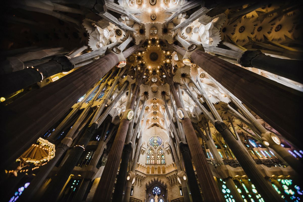 Antoni Gaudí's famous church La Sagrada Família with its beautiful ceiling and support beams on display, providing a close view of its geometric patterns and intricate details that evoke the feeling of trees and nature.