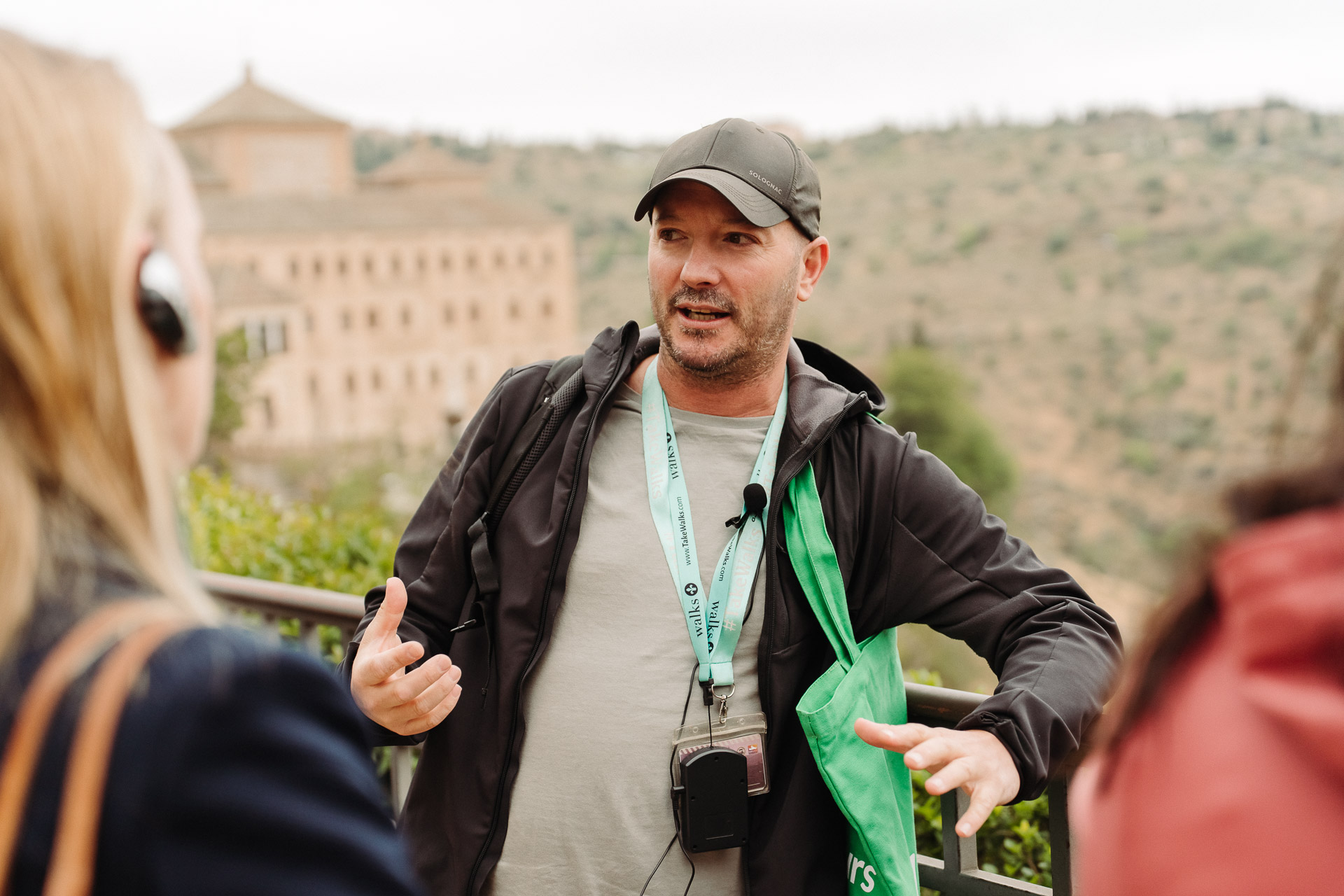 Walks tour guide with green tote bag and microphone explains Toledo to guests