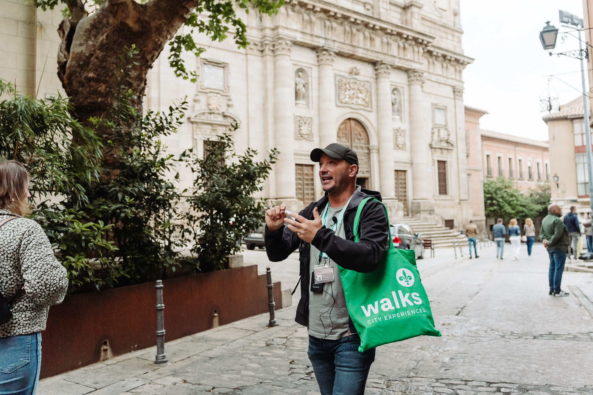 Walks tour guide with green tote bag leads guests through the streets of central Toledo, Spain
