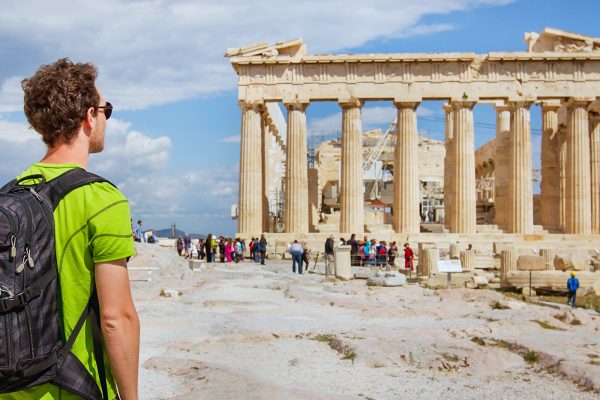 Man with a backpack and sunglasses looks out at the Acropolis in Athens, Greece