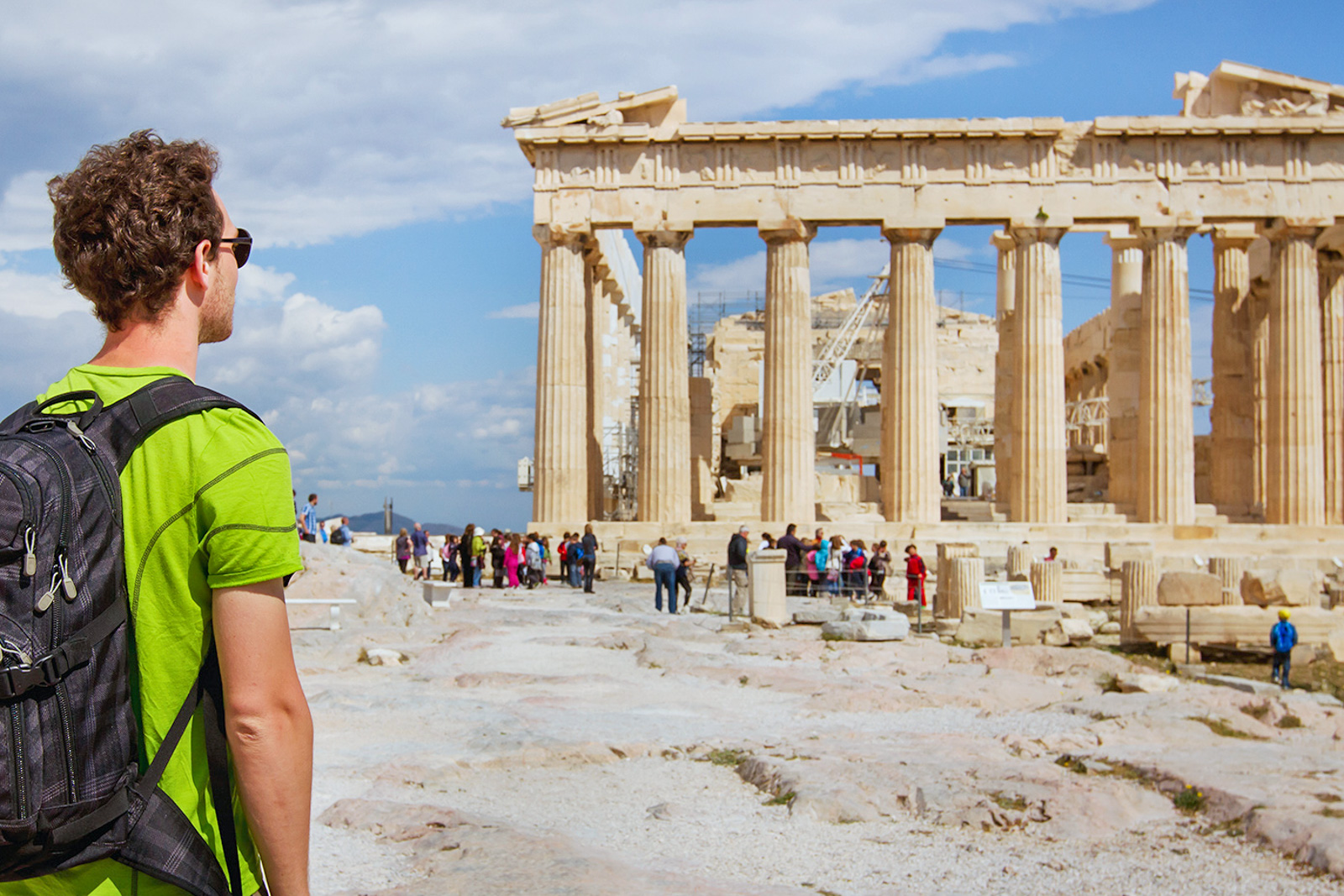Man with a backpack and sunglasses looks out at the Acropolis in Athens, Greece