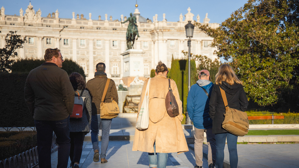 Tour group walking through Madrid's Plaza del Oriente gardens with statue and view of the Royal Palace in the background