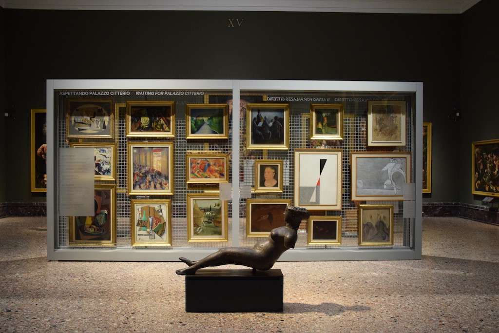 Dark museum gallery at Milan's Pinacoteca di Brera with a reclinding statue and collection of framed paintings