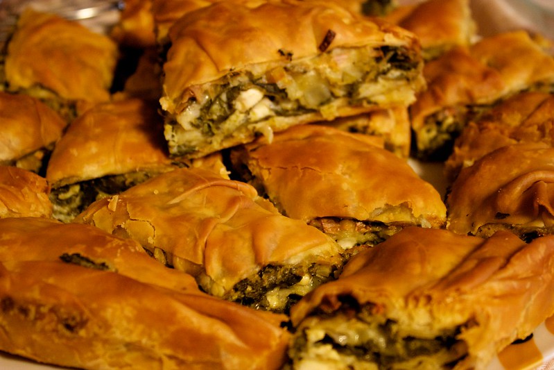 A close up image of a Greek spinach pie (Spanakopita), cut into pieces.