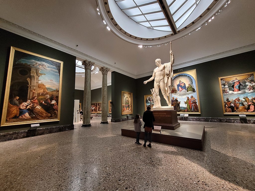 Wide-angle shot of a gallery with paintings and statue in Milan's Pinacoteca di Brera