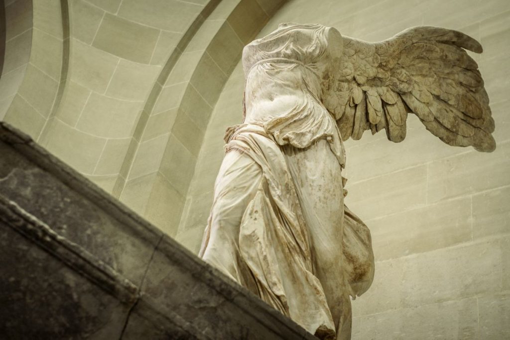 The Winged Victory of Samothrace stands headless and armless with detailed wings and draped robes at the Louvre Museum.
