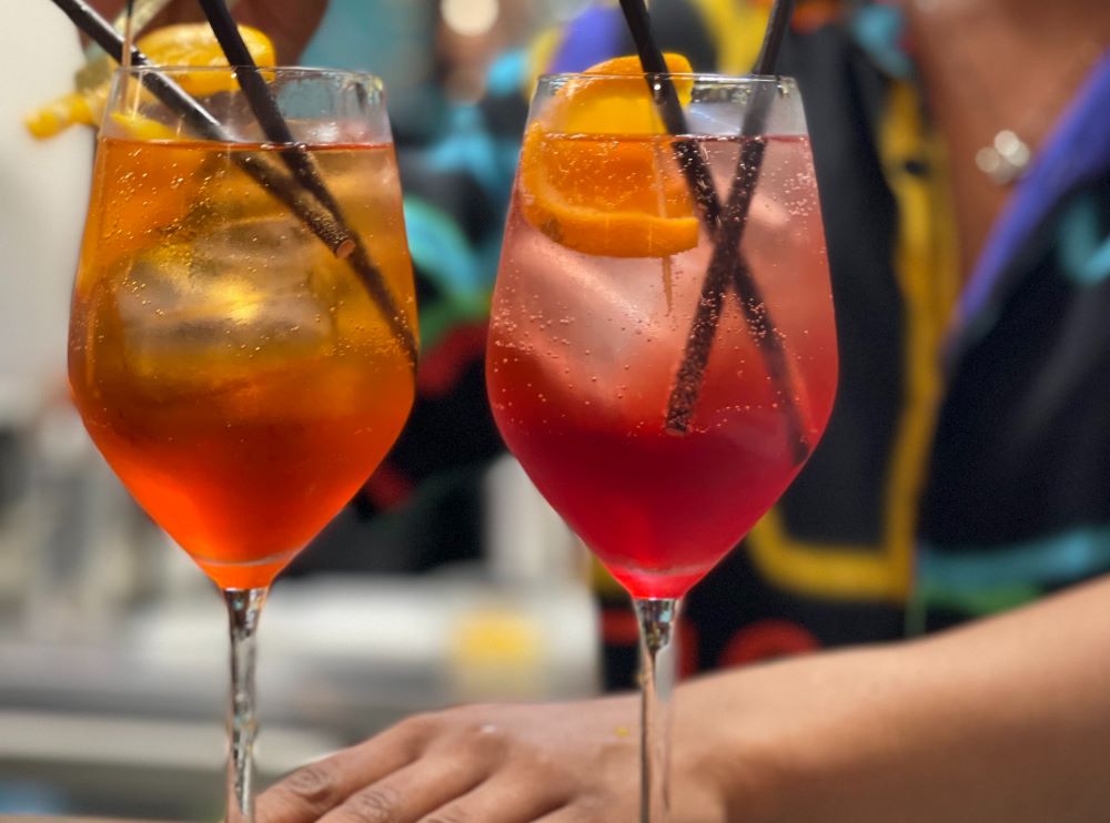 An Aperol Spritz and a Campari Spritz sit side by side on a bar.