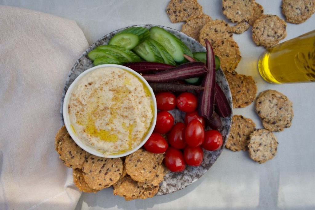 A plate of food including hummus, cherries, cucumbers, carrots and crackers.