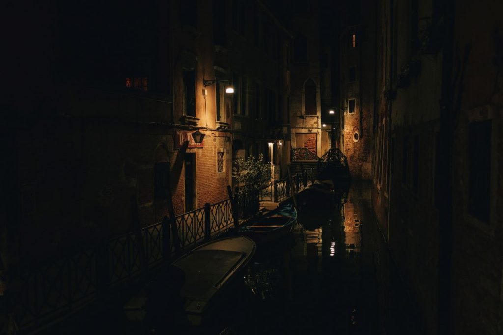 Several empty gondolas floating in a canal at nightime in Venice.