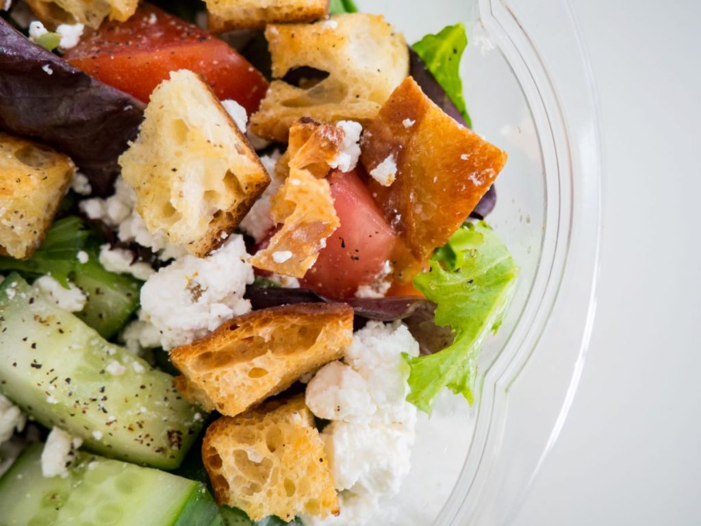 A bowl of salad including bread, cucumber, feta, tomato and lettuce.