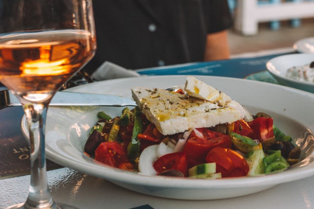 A plate of greek salad alongside a glass of wine.