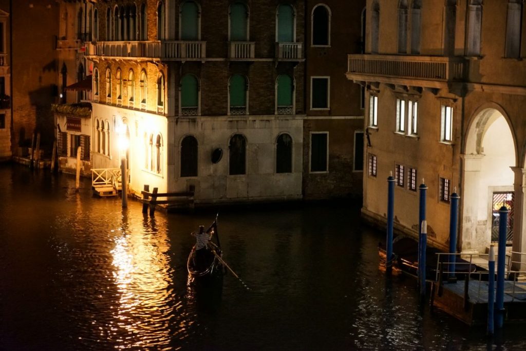 A gondolier operating a gondola on the canal at nighttime in Venice.