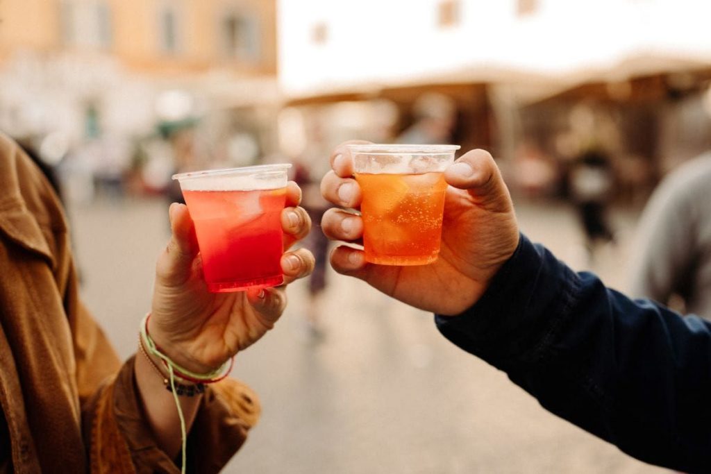 Two people toast with vibrant drinks at a sidewalk café in Piazza del Duomo, Milan, during a lively evening aperitivo.