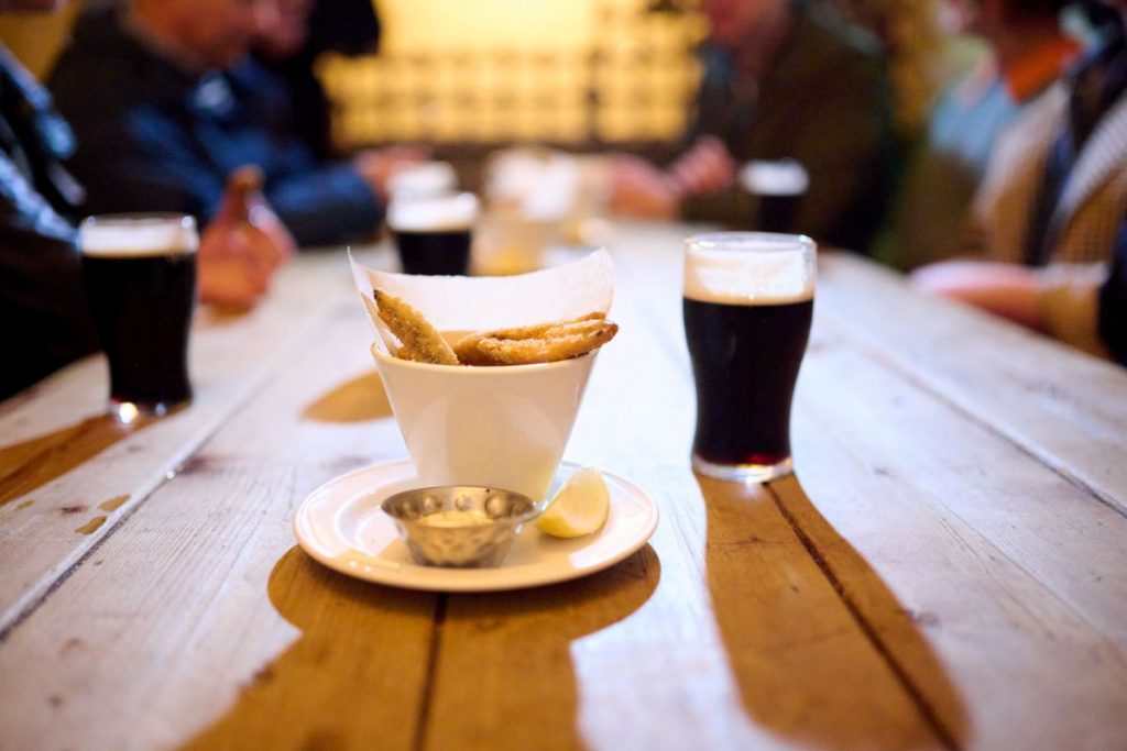 Two small pints of beer and a cup of small snacks sitting on a table