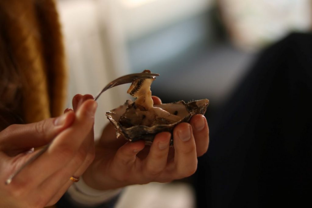 Someone holds an oyster in their hand and eats it with a fork