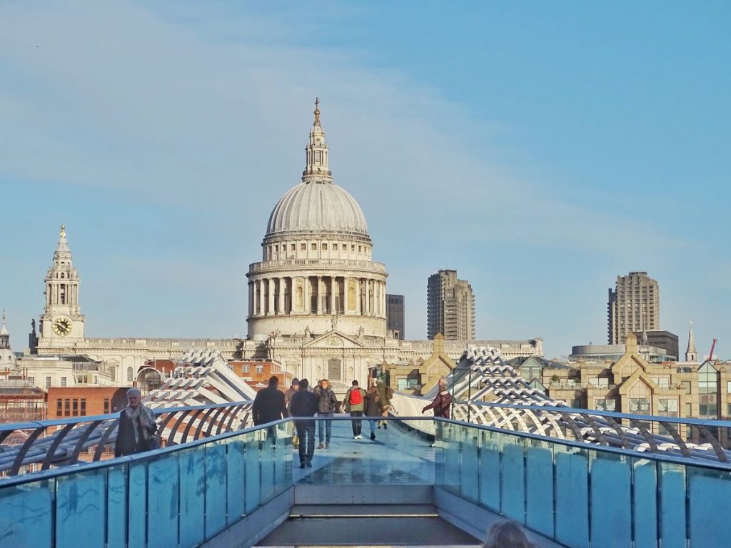 People walking on a small bridge with views of St. Paul's Cathedral in London in the background