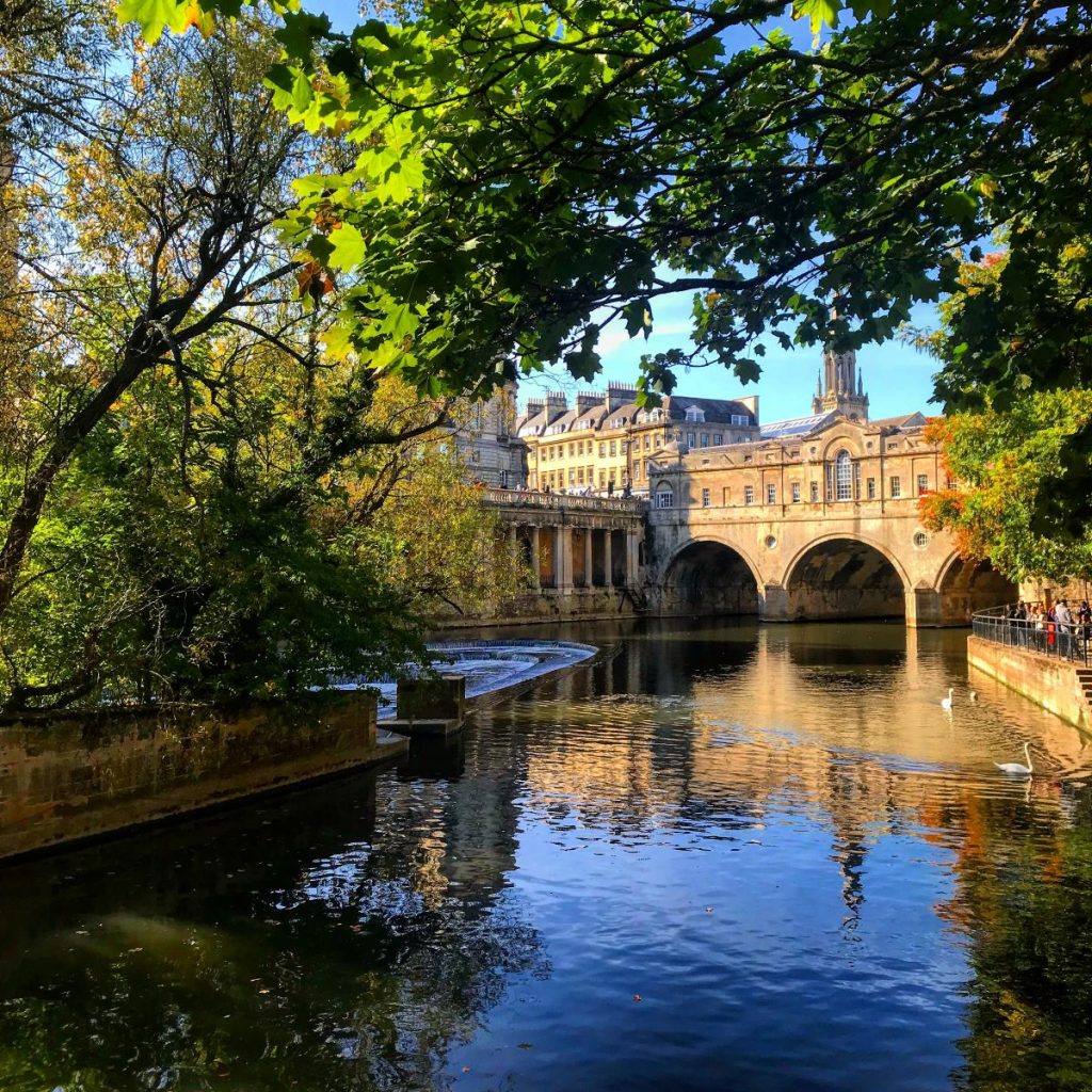 A view of a central lake and building in Bath, UK on a sunny day
