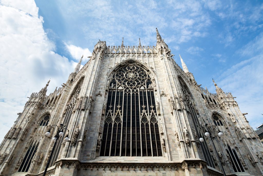 The ornate gothic facade of Milan’s Duomo features pointed arches, spires, intricate stonework, and a large rose window.