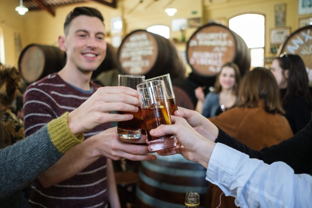 Group of four friends raise glasses of vermouth in a toast inside of a bar in Sevlle