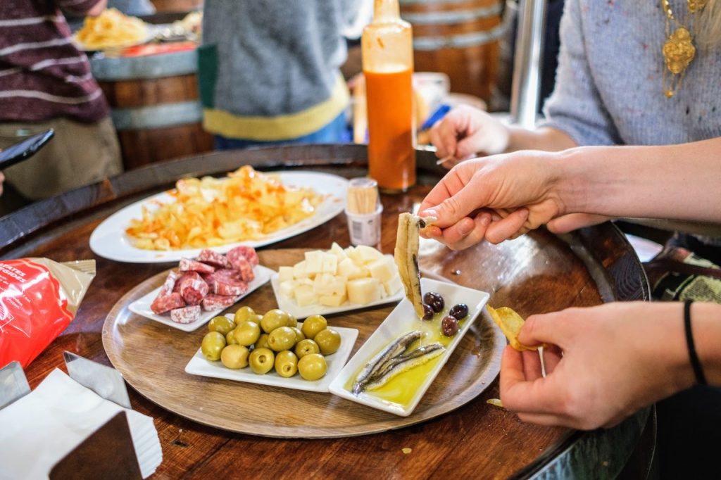 Repurposed wine barrel serves as a table top filled with Spanish tapas such as anchovies, potato chips, olives, cured meats, and cheese.