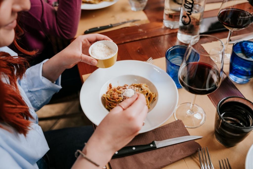 A person enjoying a plate of pasta with a glass of red wine