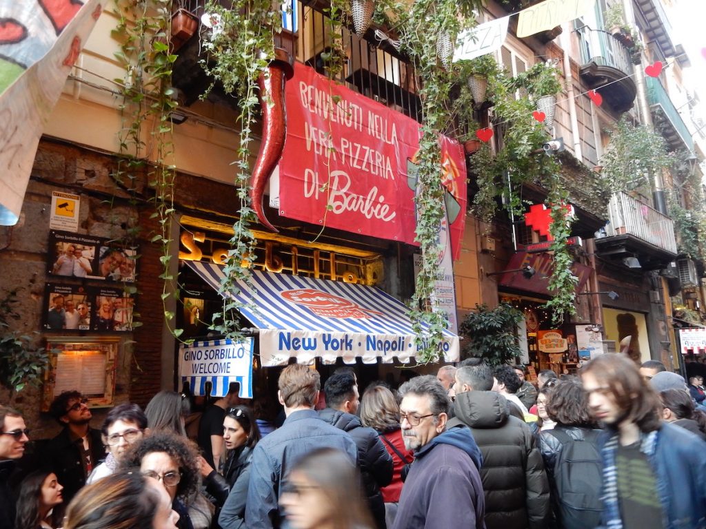 people waiting in line outside a pizza shop