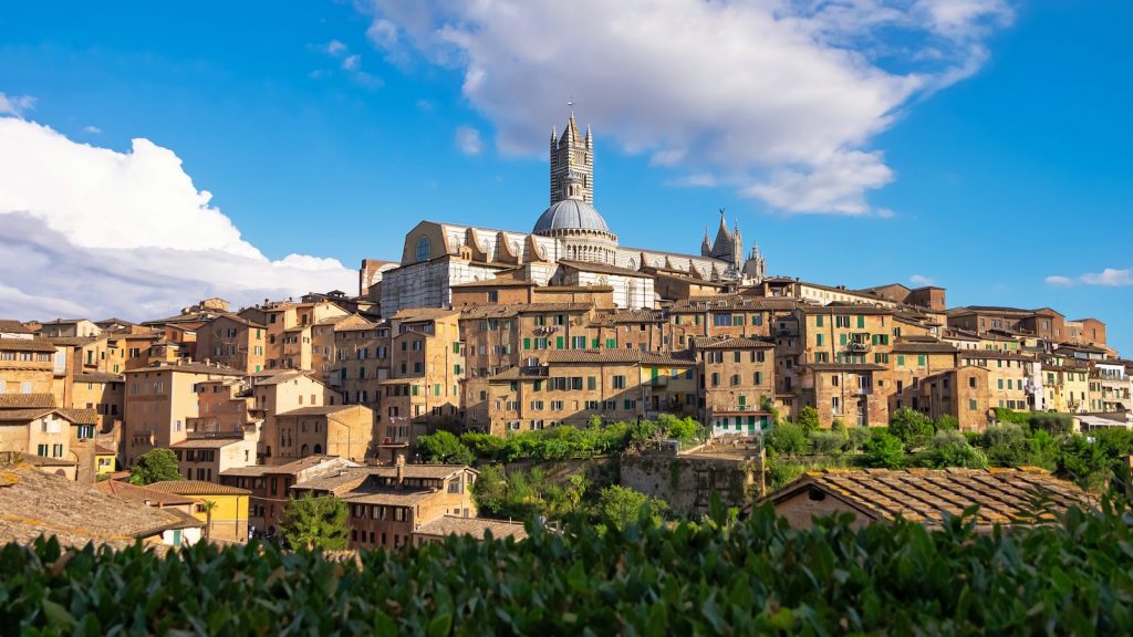 The city of Siena under blue sky during daytime, with the Duomo