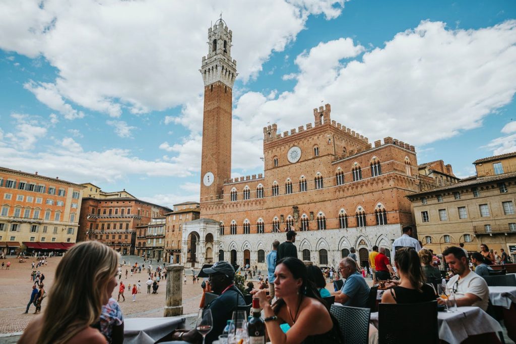 Torre del Mangia in Siena from a terrace with people sitting, sunny day