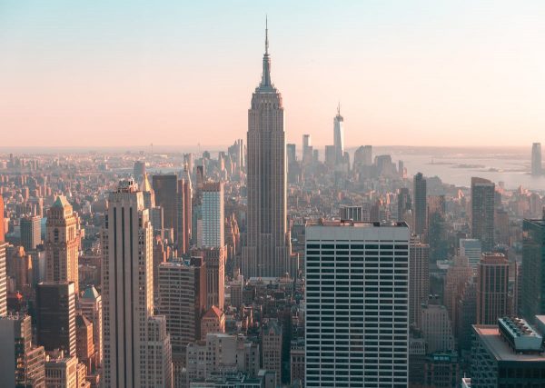 The sun sets over New York City; the Empire State Building stands central, surrounded by skyscrapers beneath a hazy golden sky.