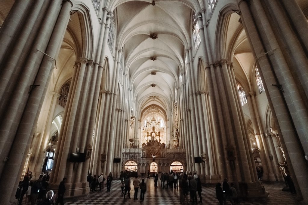 Toledo Day Trip and Winer Tour - Visitors walk beneath towering stone columns and vaulted ceilings of a grand, sunlit cathedral, admiring its ornate altar and architecture.