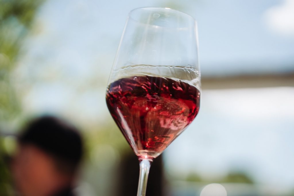 A glass of red wine being swirled in a glass on a sunny day.